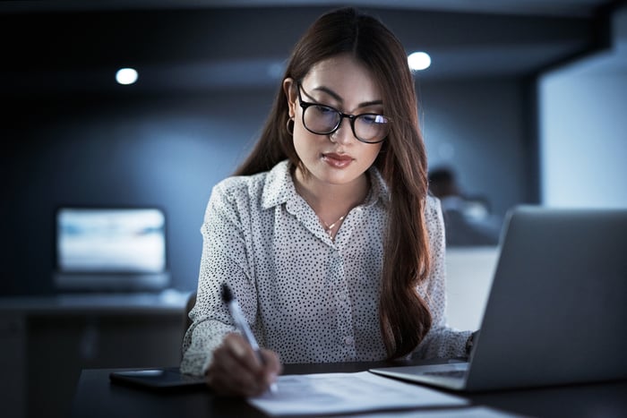 An accountant sitting in an office in front of a computer and writing on a document.