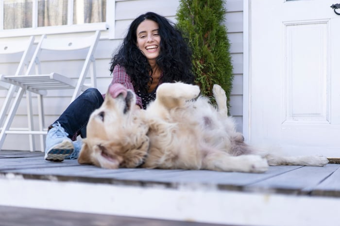 Youngish woman with long dark hair playing with Golden Retriever dog on front porch of a house.