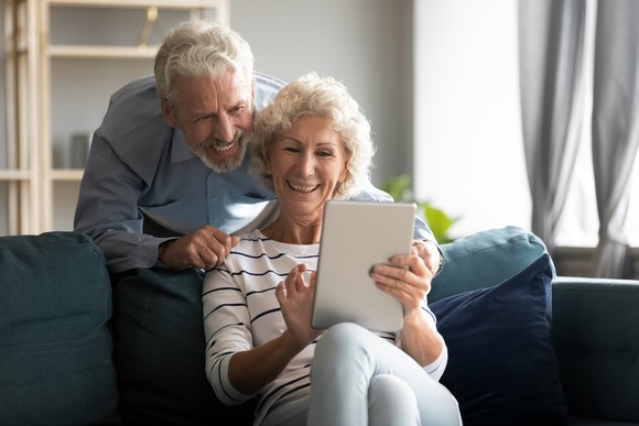 Happy retired couple smiling at a tablet.
