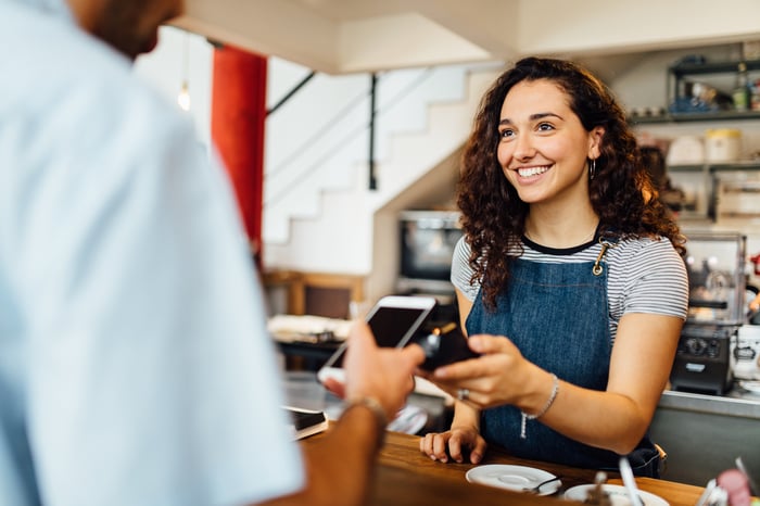 A person holding a credit card terminal next to a phone a person is using to make a contactless payment.