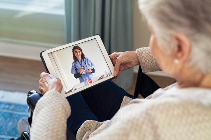 Older person in wheelchair holding a tablet showing a healthcare professional.