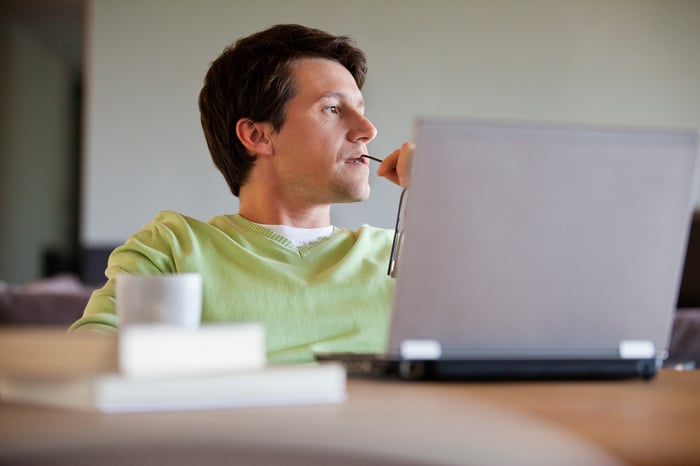 Person at laptop holding eyeglasses tip against mouth