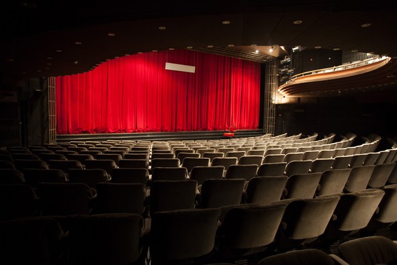 Empty movie theater with a closed red curtain in front of the screen.