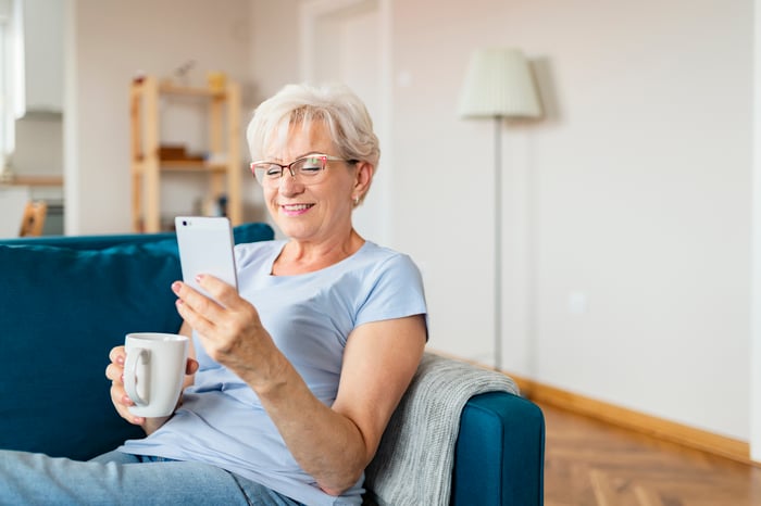 Smiling senior with coffee mug, looking at smartphone.