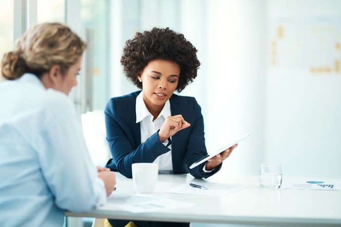 Two business people sitting in an office reviewing info on a tablet.