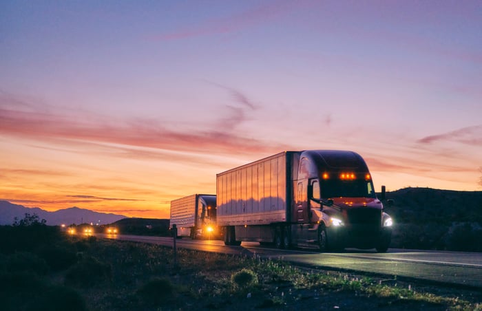 A semi truck hauls freight on an open highway at dusk.