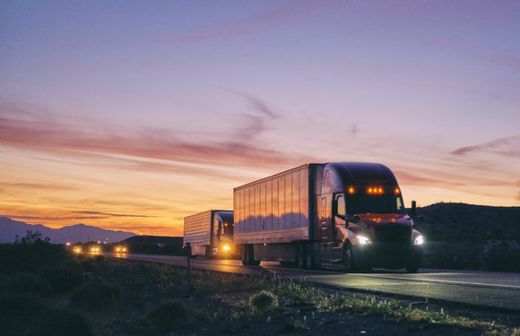 A semi truck hauls freight on an open highway at dusk.