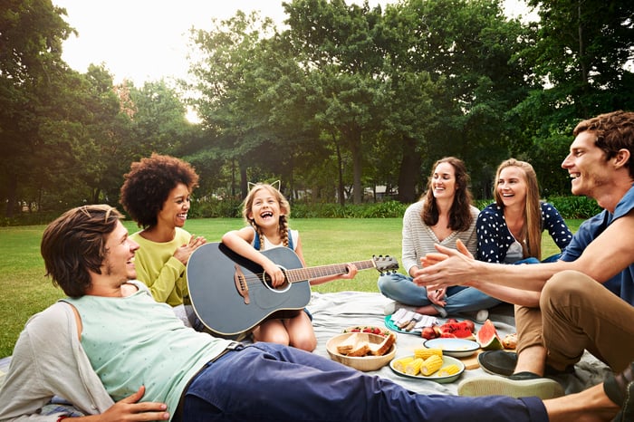 Five adults at an outdoor picnic watching young child play a guitar.