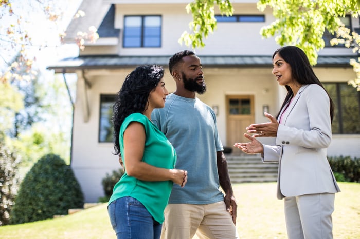 A couple meeting with a real estate agent in front of a two-story house.