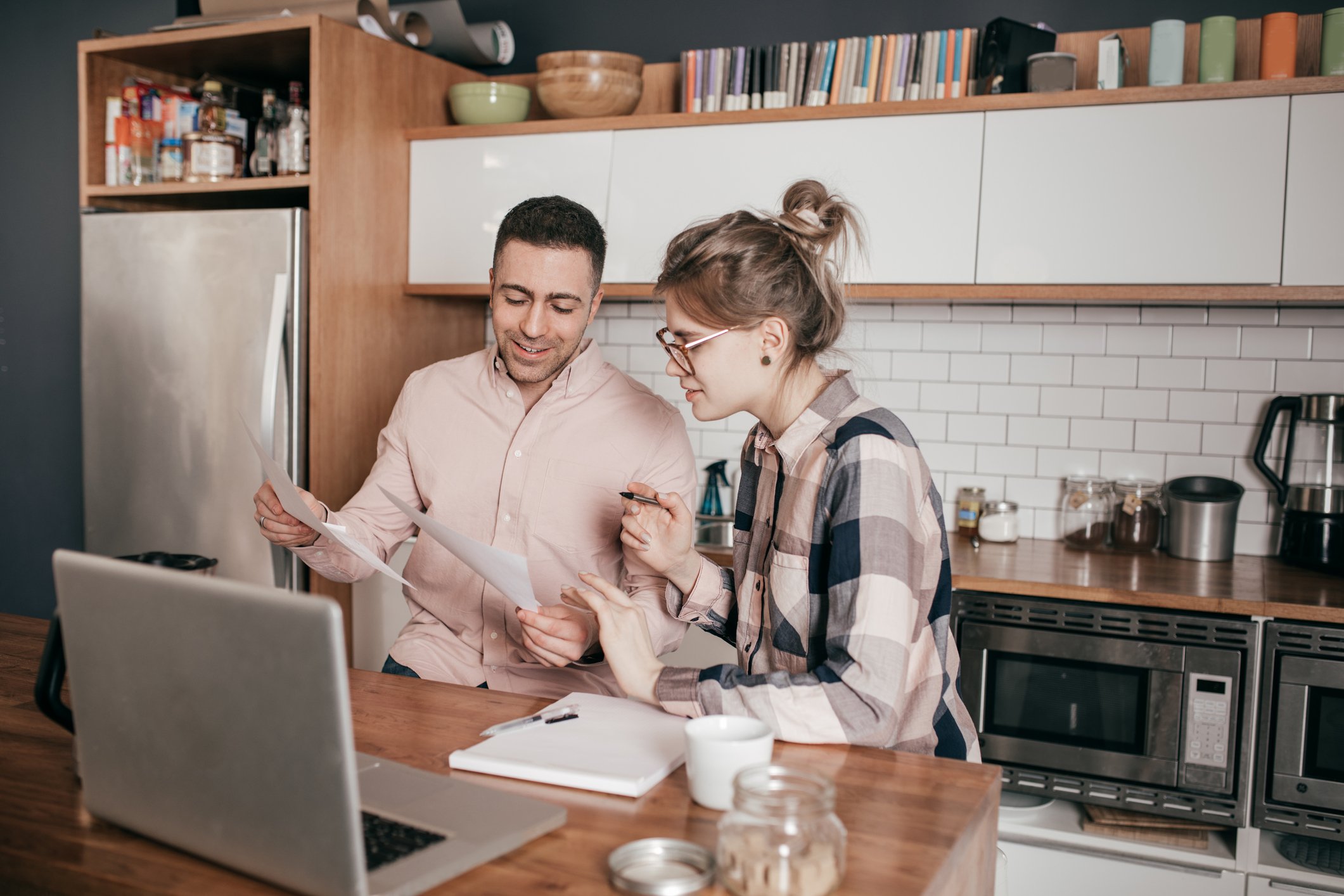 two people review documents in front of a laptop at a kitchen counter.