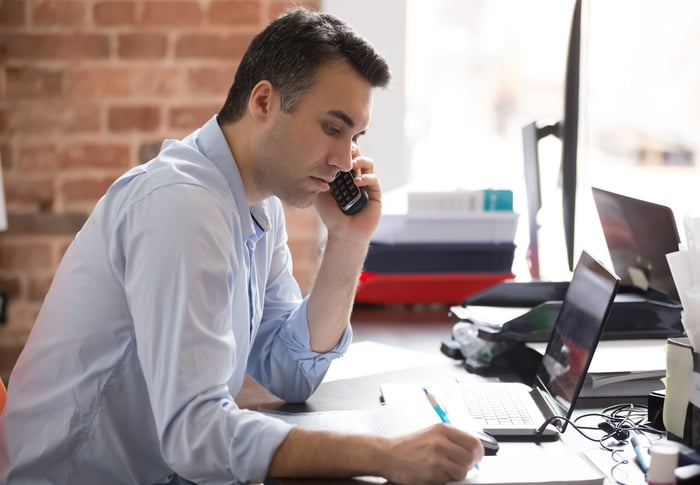 Person at desk holding phone and taking notes