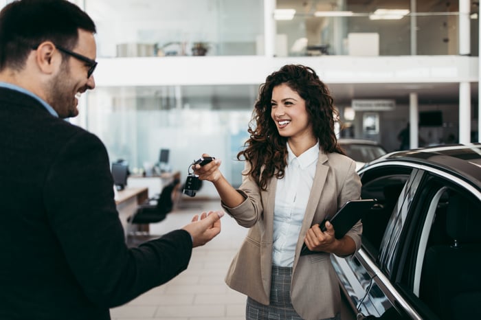 A happy buyer and seller exchanging keys at a car dealership