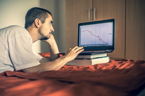 A man looks at a falling red line graph on a laptop.