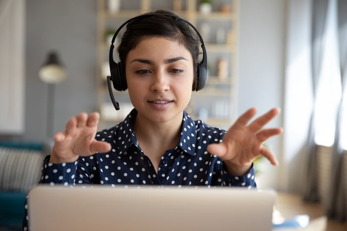 Woman wearing headset gesturing with hands at laptop