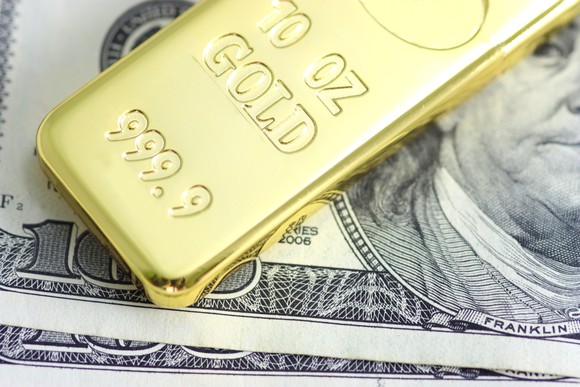 A gold bar rests on a one hundred dollar bill.
