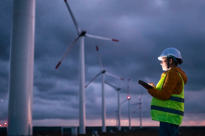 A person holding a tablet looking at wind turbines.