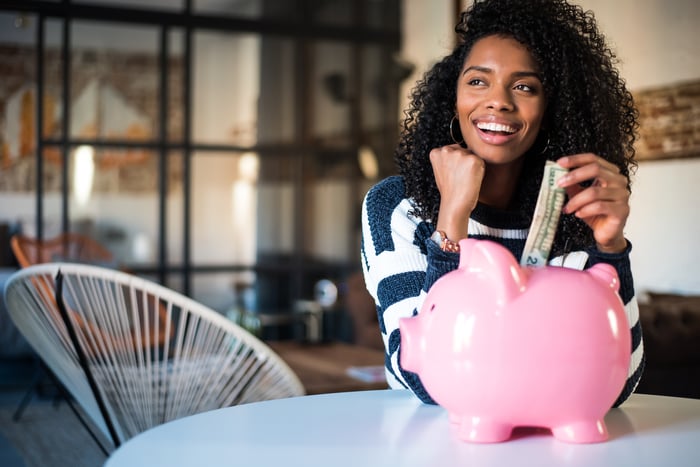 Young person putting a dollar into a piggy bank.