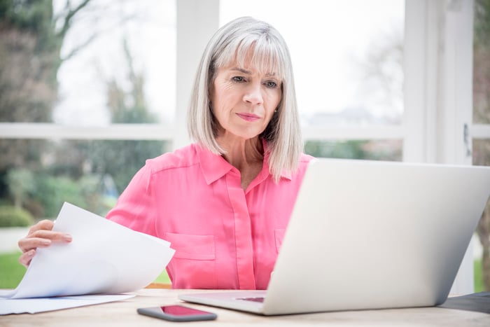 Serious senior holding papers and looking at laptop