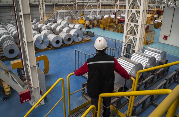 Worker wearing hard hat viewing factory floor with rolls of aluminum.