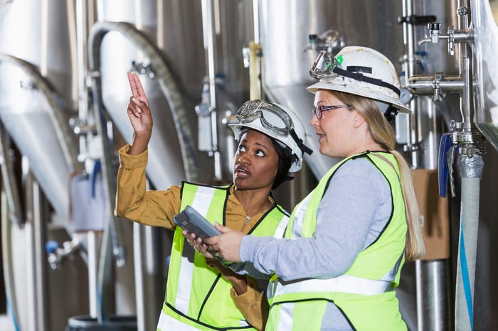 Two chemical plant workers in protective gear consulting with each other about a task.