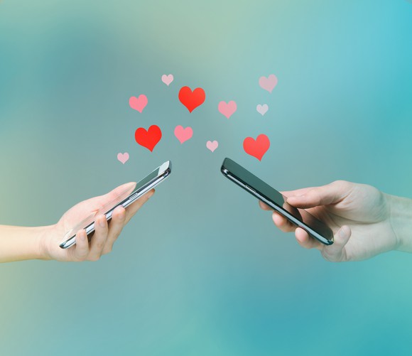 Two people holding mobile devices with heart graphics emerging from them.