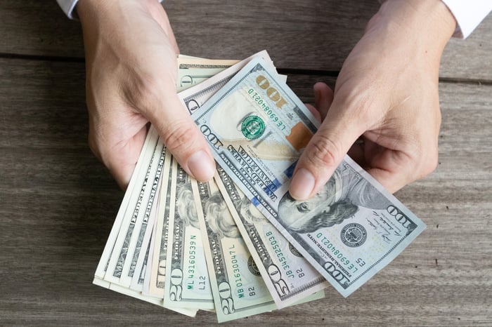 A person holding a fanned assortment of cash bills. 