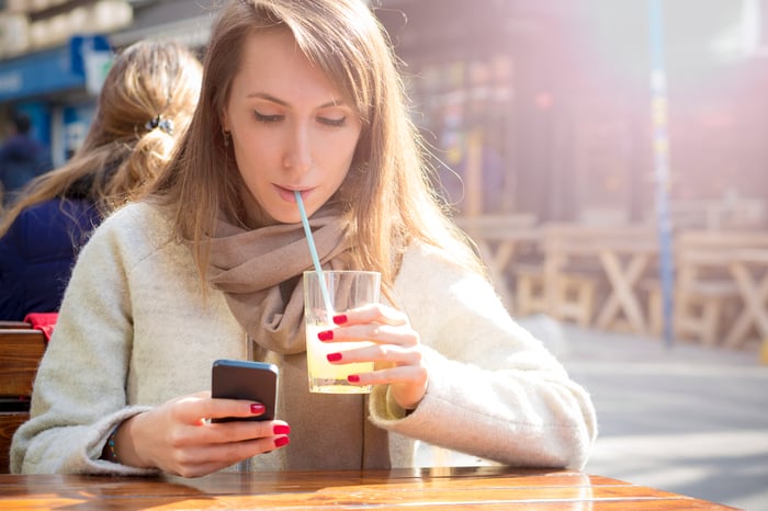 A smartphone user sips lemonade.