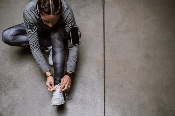 A person in workout clothes sitting on the floor and tying her shoelaces.