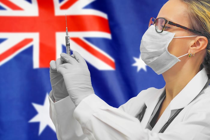 Healthcare professional holding a syringe with needle in front of an Australian flag.