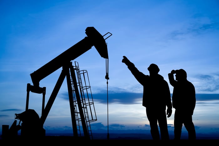 Silhouette of two people pointing to an oil well.