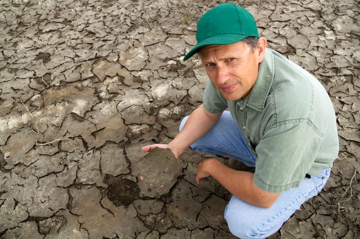 Farmer in a dry field holding up a large piece of cracked soil.