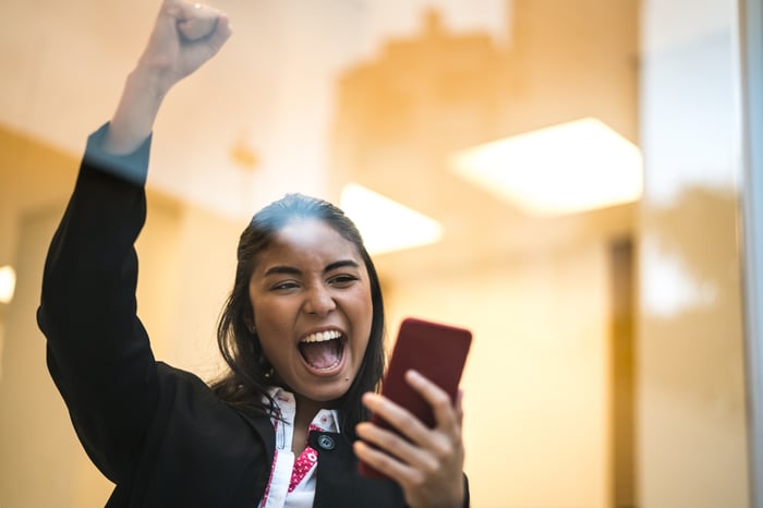 A businesswoman celebrates while looking at her smartphone.