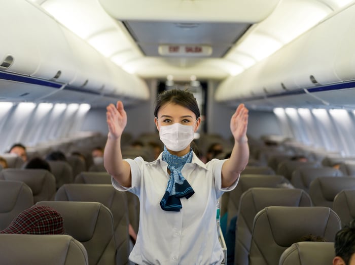 A flight attendant in a mask giving safety briefing on an airplane.