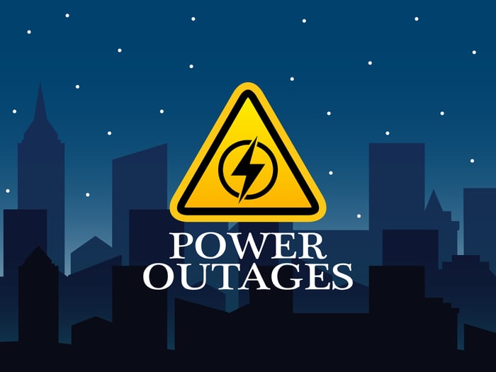 "Power outages" yellow warning sign with a darkened cityscape in background.