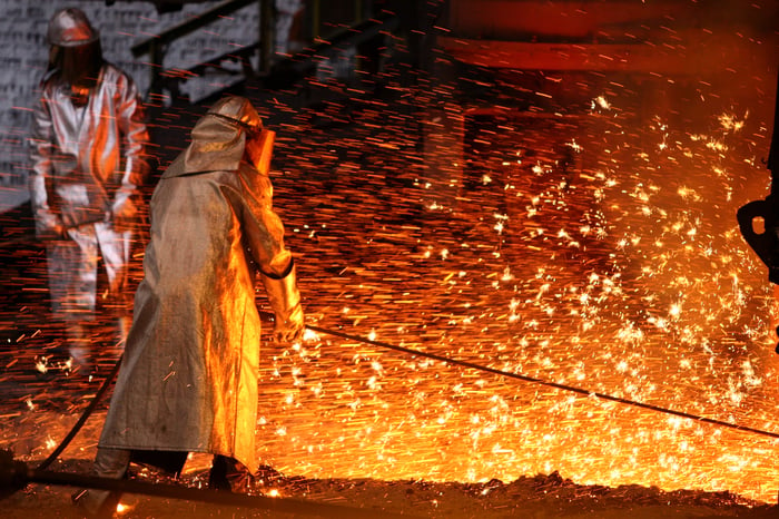 Two workers in full protective gear in a steel smelting facility.