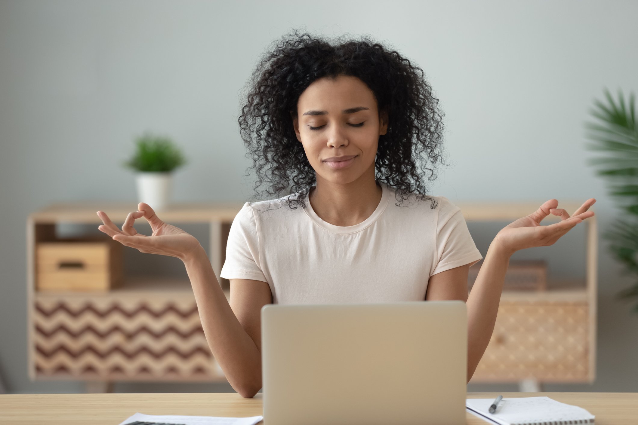 A relaxed woman meditating sitting at a desk in front of a laptop