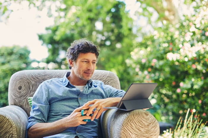 Man sitting in chair outdoors looking at tablet