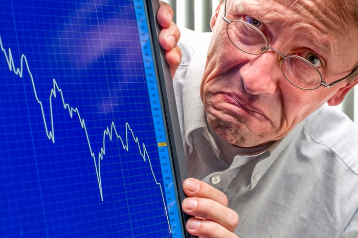 A frowning person next to a stock chart on a computer screen depicting a market crash.