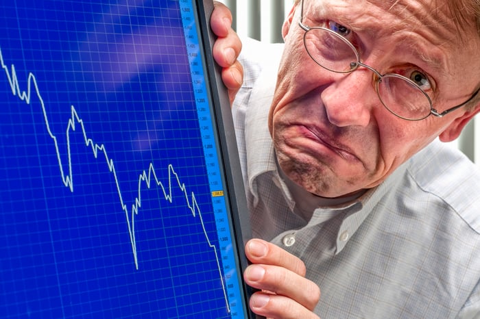 A frowning person next to a stock chart on a computer screen depicting a market crash. 