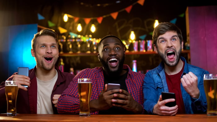 Three people in a pub holding their smartphones.