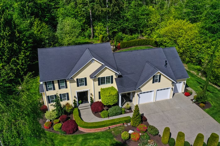 Aerial view of a beautiful two story house surrounded by green foliage.