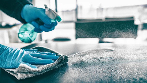 Gloved hands with washcloth and spray bottle cleaning a countertop.