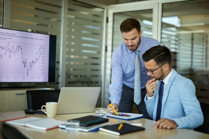 Two workers analyze a financial chart in an office.