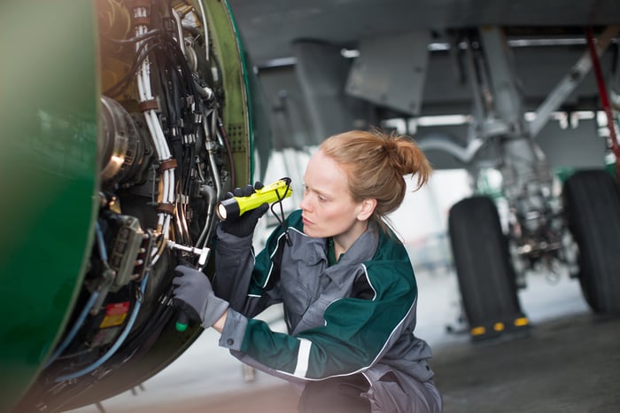 Engineer using flashlight to analyze airplane part.