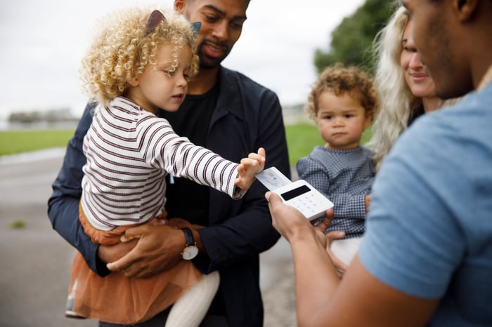 Child in parent's arms using a credit card to pay for something