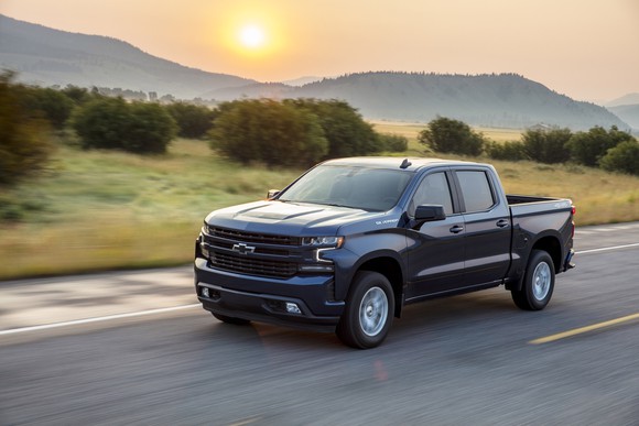A black Chevy Silverado driving on a road, with a blurred green field in the background.