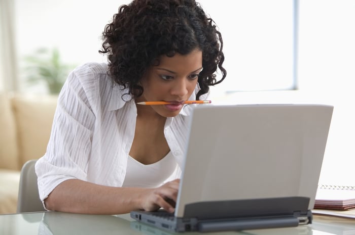 A person with a pencil in their mouth working frantically on a laptop.