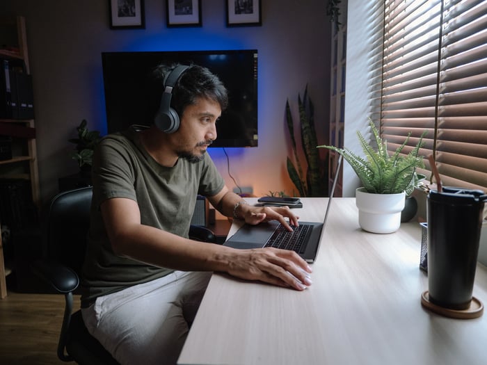 Young person wearing headphones navigates on a laptop while sitting at a desk.