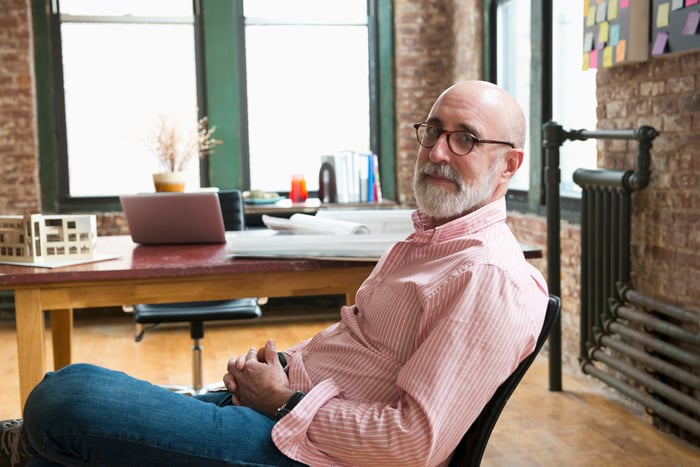 Senior person leaning back in chair in front of desk.