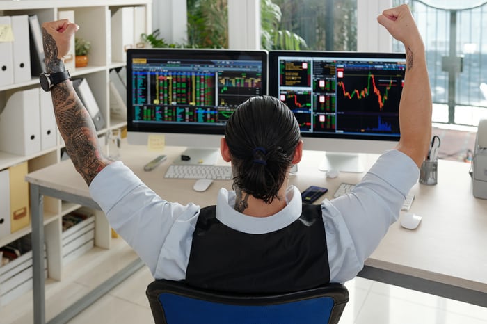 A person raising his hands in celebration while studying stock price charts on computer screens.